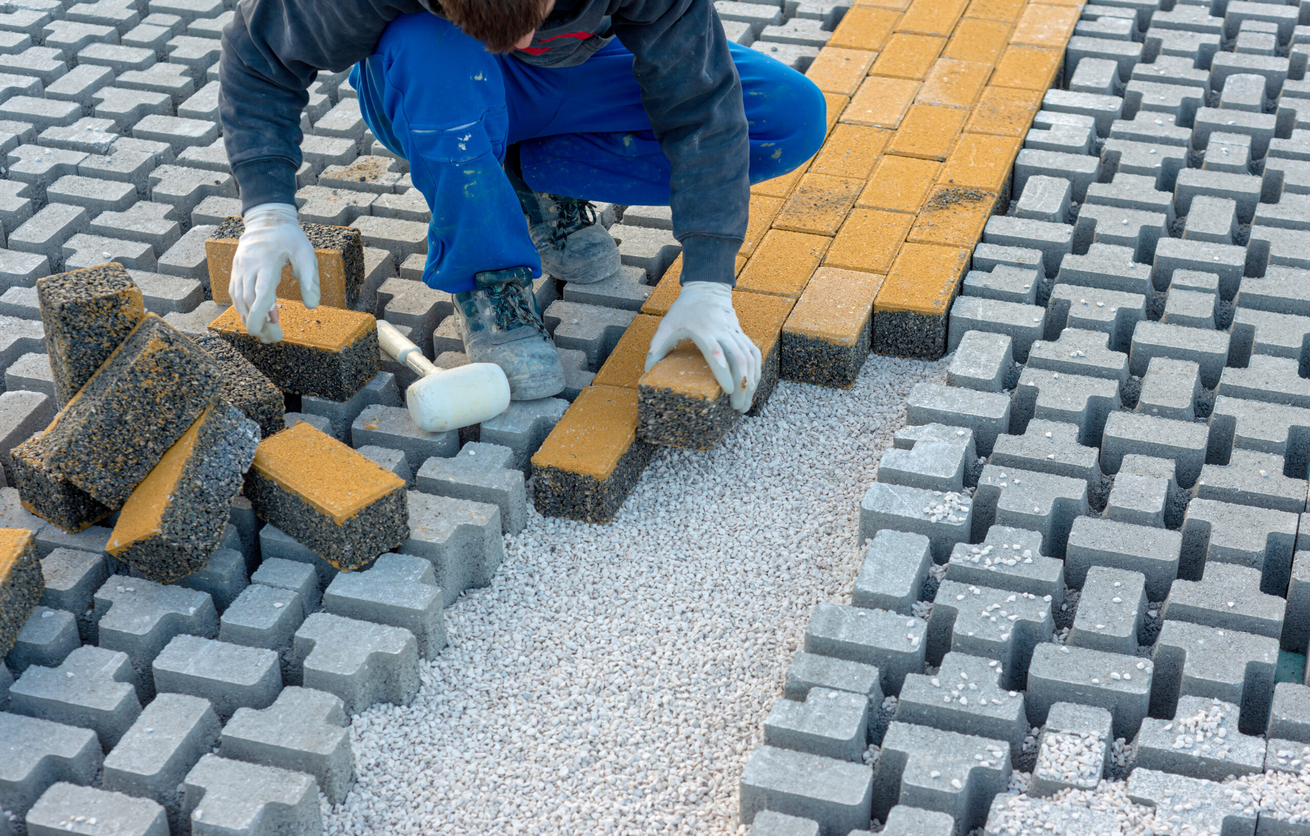 Paving stone worker is putting down pavers during a construction of a city street onto sheet nonwoven bedding sand and fitting them into place.